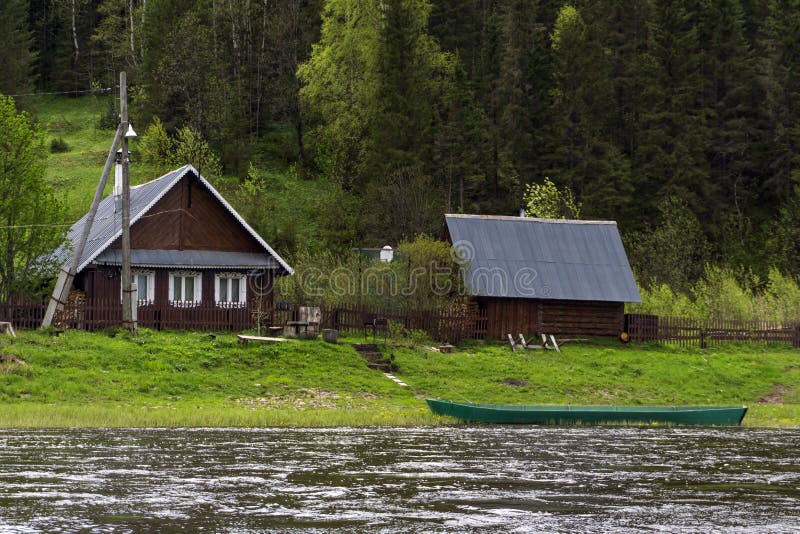 Traditional russian village house on the river bank. Traditional Russian wooden village house and a courtyard by the river in a hilly wooded area stock image