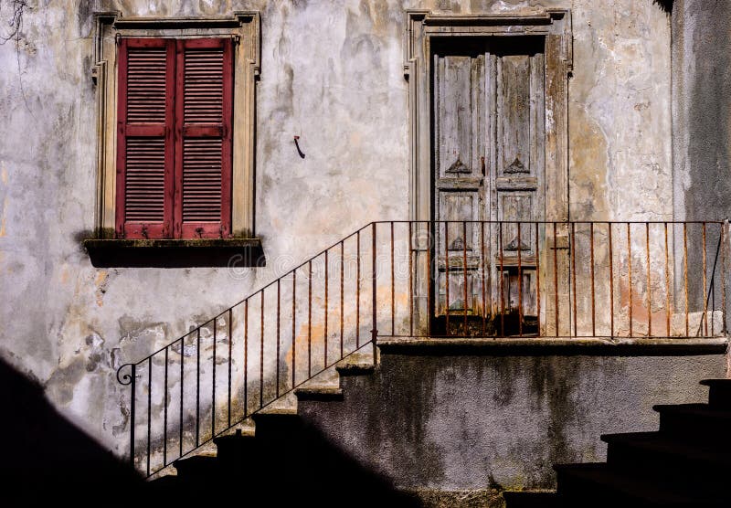 Traditional sun-lit rustic Italian architecture facade with stairs alongside iron railing leading to worn out stairs and wooden do. Or stock photography