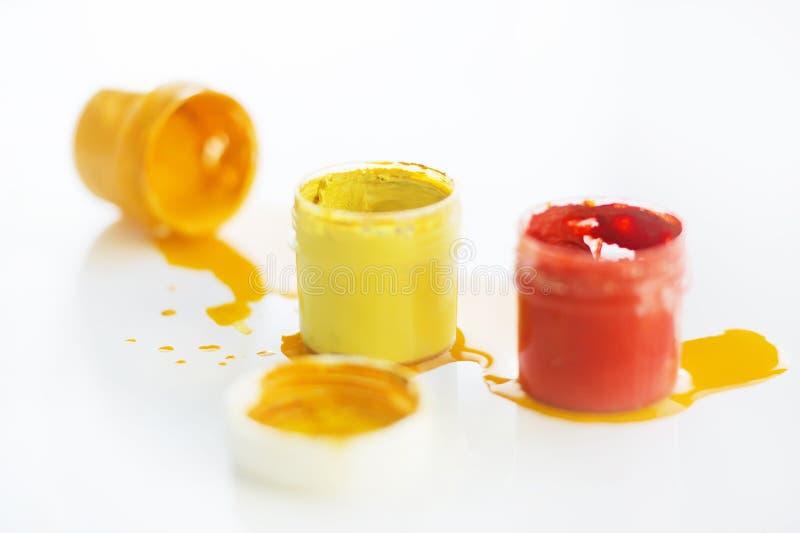 Two jars of gouache are yellow and red colors , and next to another jar fell and the paint flows out of it royalty free stock photo