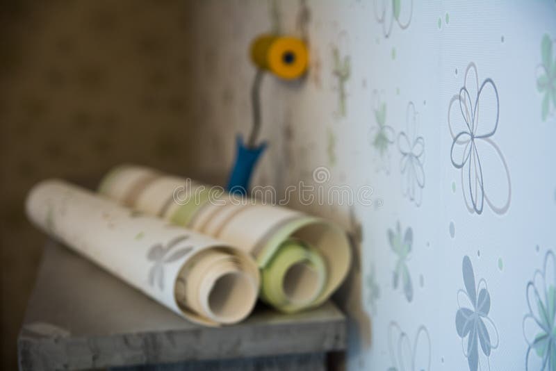 Two rolls of wallpaper and a roller lie against. The wall with floral wallpaper stock photo