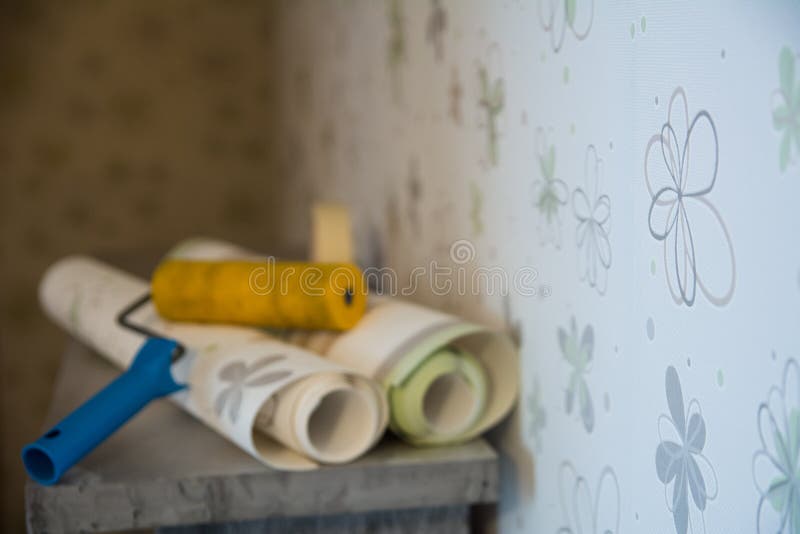 Two rolls of wallpaper and a roller lie against. The wall with floral wallpaper. Focus on the wall with a flower royalty free stock image