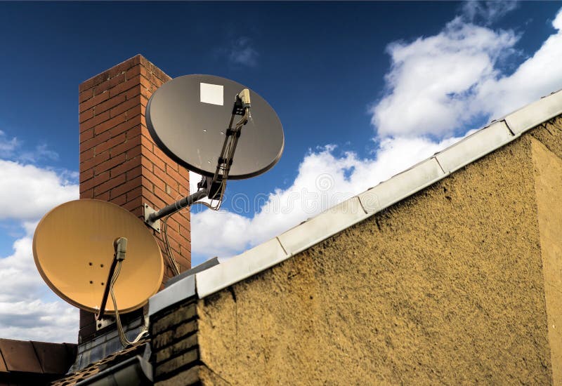 Two satellite dishes in front of a red brick chimney on the sloping roof of a house. Germany royalty free stock photos