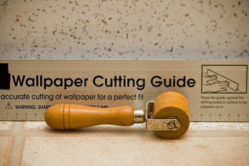 Vintage wallpaper seam roller. A vintage wallpaper seam roller in front of a wallpaper cutting guide stock images