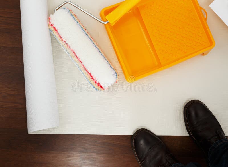 Wallpaper with roller and painting tray. Man shoes near lying wallpaper with roller and painting tray on it stock photo