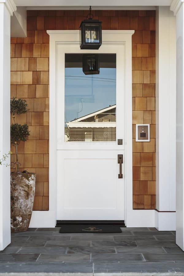 White front door to a luxury home. A white front door of a luxury home. The home is naturally stained wood shingles. The door is flanked by two white columns stock photos
