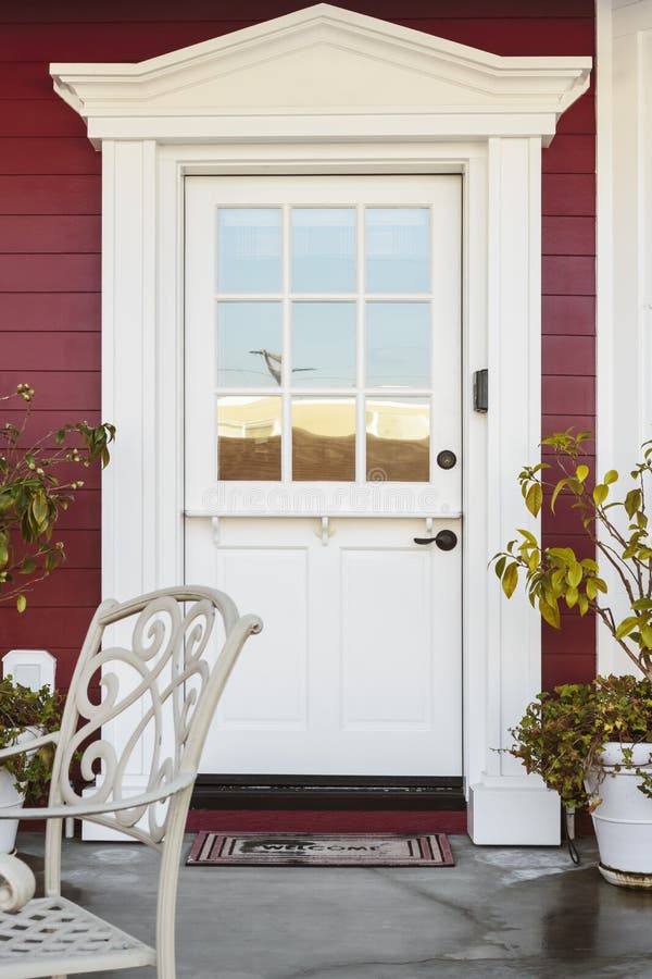 White front door of an upscale home. A white front door of an upscale home. Also seen is red siding, plants, and a patio chair royalty free stock images
