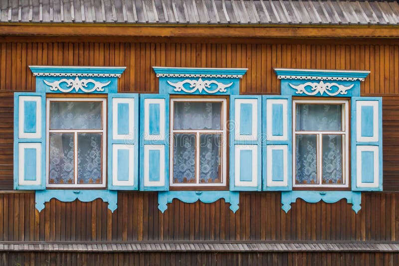 3 windows with beautiful blue platbands, shutters and white curtains in a wooden house royalty free stock photos