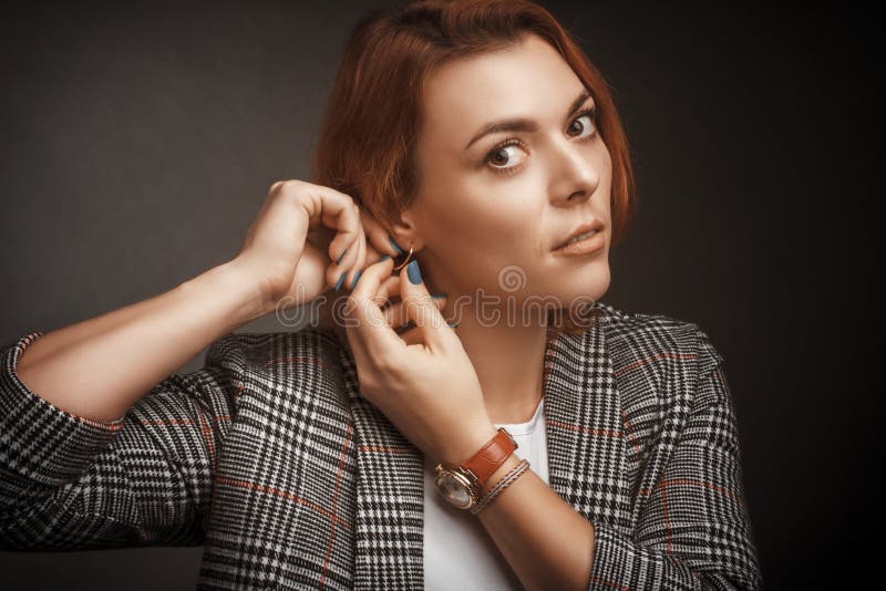 A woman fastens an earring, looking into the frame, Studio portraitwarm colors. A woman fastens an earring, looking into the frame, a Studio portrait in warm stock image