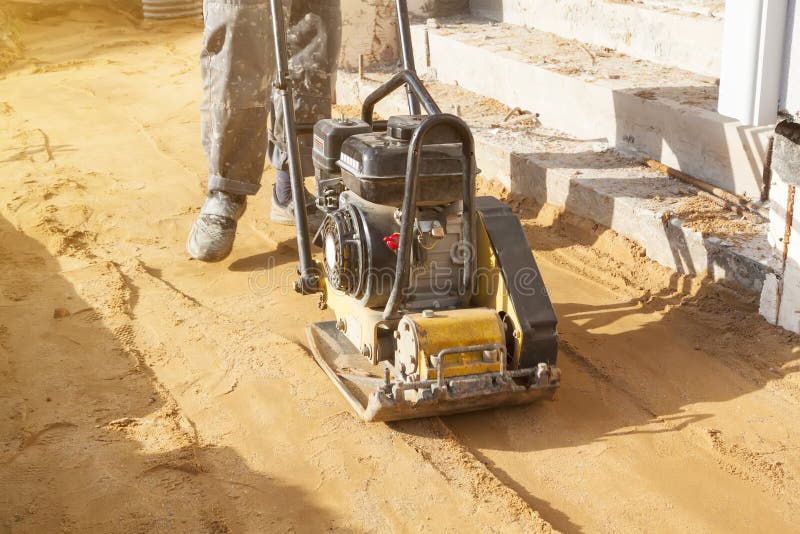 Worker compresses sand in blind area around building with special working tool & x28;tamping machine royalty free stock image