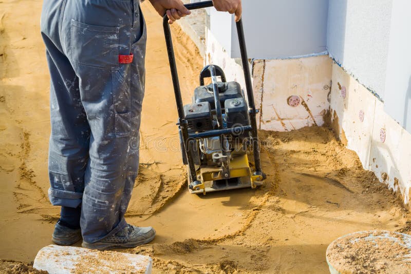 Worker compresses sand in blind area around building with special working tool & x28;tamping machine or vibratory plate stock images