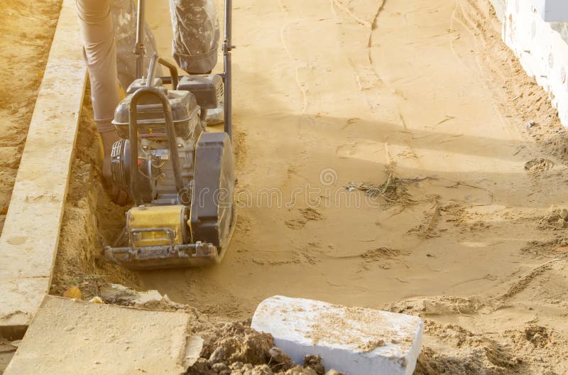 Worker compresses sand in blind area around building with special working tool & x28;tamping machine or vibratory plate stock images