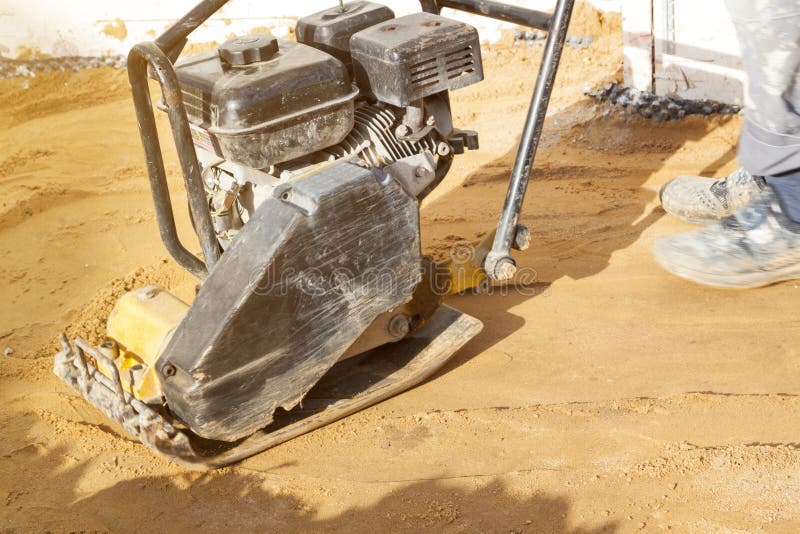 Worker compresses sand in blind area around building with special working tool & x28;tamping machine royalty free stock photo