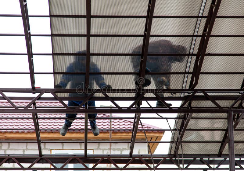 A worker mounts a metal canopy in the courtyard of the house. Silhouette man bottom view stock images