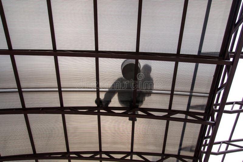 A worker mounts a metal canopy in the courtyard of the house. Silhouette man bottom view royalty free stock photo