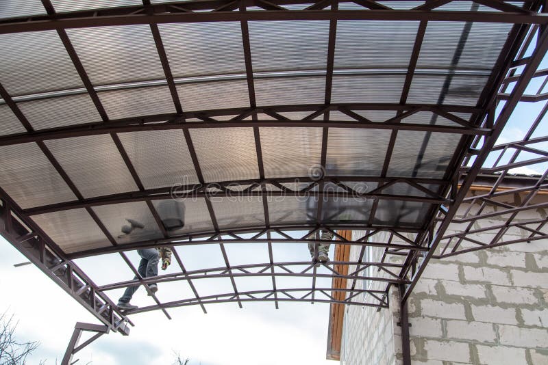 A worker mounts a metal canopy in the courtyard of the house. Silhouette man bottom view royalty free stock photography