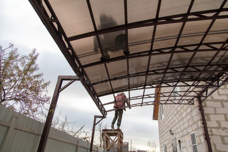 A worker mounts a metal canopy in the courtyard of the house. Silhouette man bottom view royalty free stock photo