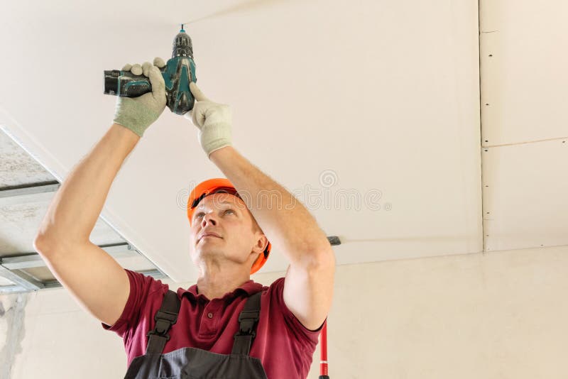 Workers are using screws and a screwdriver to attach plasterboard to the ceiling. Installation of drywall. Workers are using screws and a screwdriver to attach royalty free stock photo