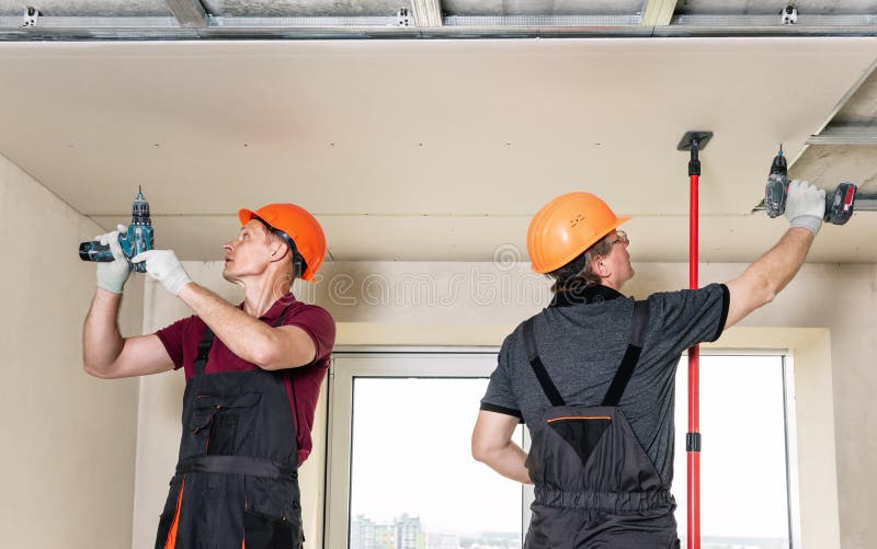 Workers are using screws and a screwdriver to attach plasterboard to the ceiling. Installation of drywall. Workers are using screws and a screwdriver to attach royalty free stock image
