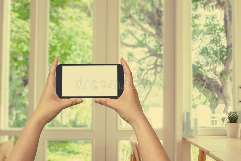  Владение руки и мобильный телефон экрана касания, мобильный над запачканным окном с взглядом сада стоковая фотография