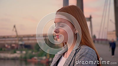 Portrait of young ginger woman standing on bridge, looking away and then in camera, smiling, sunset stock video